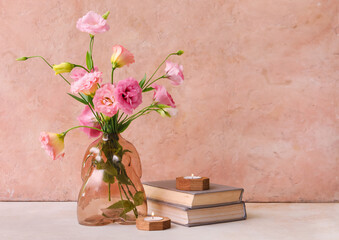 Vase with beautiful pink eustoma flowers, books and candles on light table