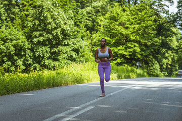 Strong athletic black woman sprinting during workout while listening to music with earphones.