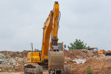 Lonely excavator in a landfill with garbage and soils. The work of construction equipment in the production of earthworks