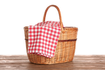 Wicker picnic basket with red checkered napkin on wooden table isolated on white background