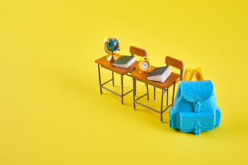 Fototapeta premium School desk with school accessory and blue backpack on yellow background