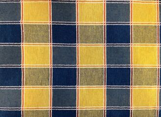 Closeup of plaid fabric, textured background of yellow blue checks or tartan pattern. Natural linen or cotton fabric cloth or napkin. Textile with red grid lines and gold and teal squares details.