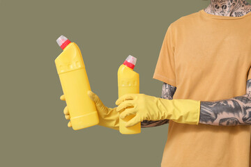 Young tattooed man with bottles of detergent on green background, closeup