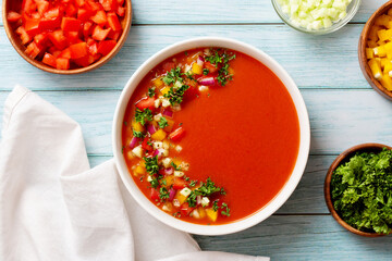 Spanish tomato gazpacho cold soup styled and decorated in white plate with ingredients on wooden...