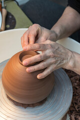 hands that work on a piece of clay that is resting on the plate of a potter's wheel