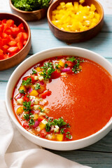Spanish tomato gazpacho cold soup styled and decorated in white plate with ingredients on wooden plank table, top view
