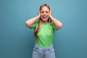 Fototapeta premium a young woman in a casual outfit covered her ears from a loud sound on a blue isolated background