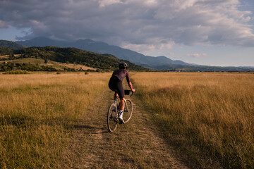 Fototapeta premium Male cyclist wearing cycling kit and helmet riding on the road a gravel bike at sunset.Sports motivation image.