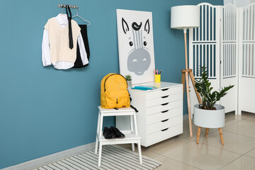 Stylish interior of children's room with school uniform, backpack and poster