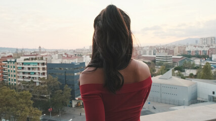 Fototapeta na wymiar Close up, young woman standing on the balcony looking at the city at sunset, back view