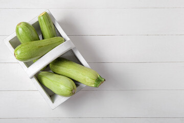 Basket with fresh green zucchini on white wooden background
