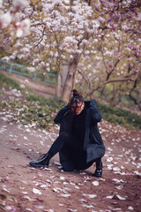 Dramatic young woman wearing black kimono and yellow glasses with cherry blossoms, sakura view
