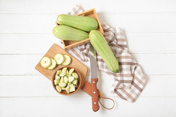 Board and box with fresh green zucchini on white wooden background