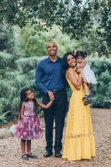 beautiful indian family standing and smiling in the park with trees and greenery