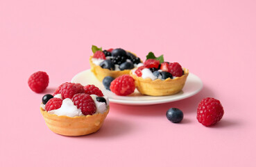 Plate of tasty tartlets with whipped cream and berries on pink background