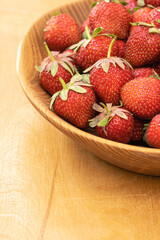 Wooden bowl full of freshly picked ripe red strawberries on the wooden background. Summer berries rich in vitamins. Healthy nutrition concept