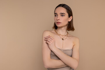 Woman wearing elegant dress and gold chain standing isolated over beige background.