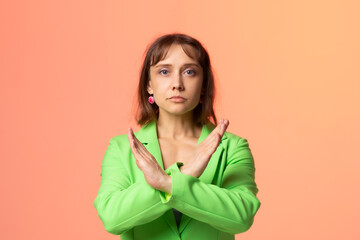 A woman in a light green suit on an orange background crossed her hands, shows a sign no, that's...