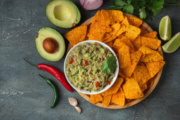 White bowl of traditional Mexican guacamole with nachos on grey concrete background. Tortilla chips...
