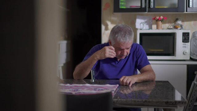 Drunk senior man dozing off while drinking alcohol at home kitchen table. Candid depicting of alcoholic elderly person