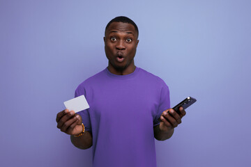 young surprised handsome american guy dressed in basic t-shirt holding bank card and smartphone