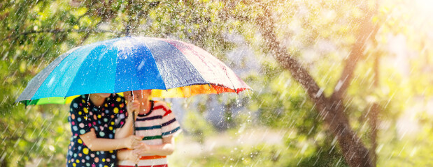 Boy and girl standing outdoors in rainy day under colourful umbrella. - obrazy, fototapety, plakaty