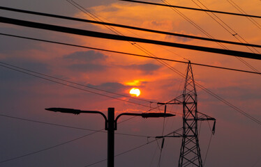 Sunset with view of the sun and high voltage cables in a city
