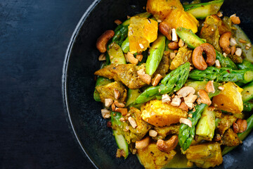 Traditional curry chicken fillet with orange, green asparagus and nuts in sweet sour vinaigrette served as top view in a design plate with text space left
