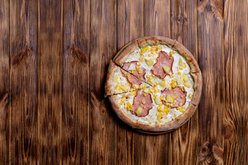 Delicious pizza with ham, pineapple, corn on a creamy base on woden background. Hawaiian pizza