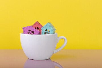House models in coffee cup over yellow background with copy space. Home buying and mortgage concept. House sale proposal