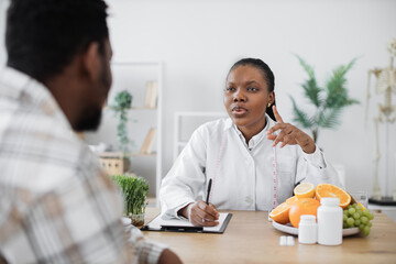 Confident female dietitian in lab coat consulting male patient in doctor's office of clinic....