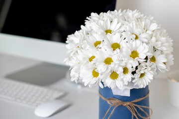 Beautiful bouquet of chamomile flowers on office desk near computer