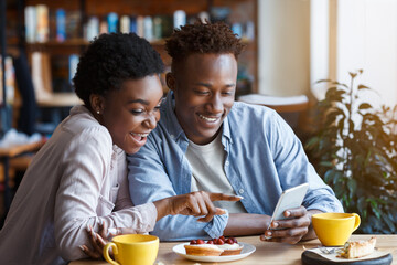 Obraz na płótnie Canvas Beautiful black couple with smartphone on date in coffee shop