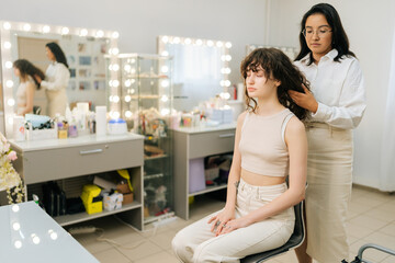 Portrait of professional female hairstylist doing stylish hairdo to long haired woman sitting on...