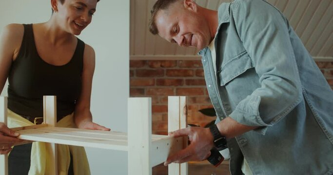 A man and a woman assemble a shelving at home, they use a screwdriver, talk and smile
