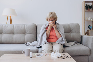 Senior woman being sick having flu sitting on sofa. Sick older lady sitting in bed with high fever.
