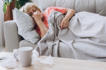 Senior woman being sick having flu lying on sofa. Sick older lady lying in bed with high fever.