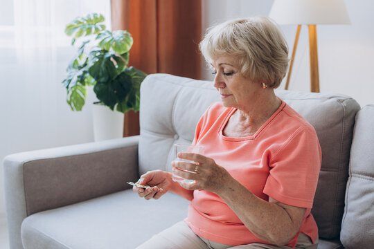 Senior Woman Wake Up Sits On Bed In Bedroom Alone Holding Glass Of Natural Water Taking Daily Pill For Good Health And Senile Disease Prevention, Memory Meds, Vitamins Concept