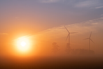 Sonnenaufgang im Nebel mit Windkraftanlagen im Hintergrund