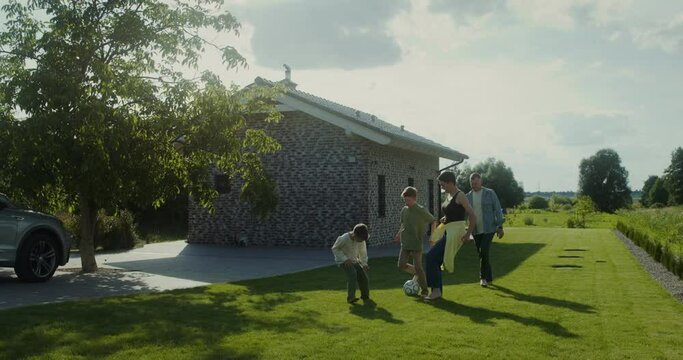A man, a woman and two children play football in the backyard of their house, family outdoor leisure