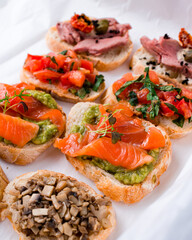 Set of snacks bruschetta with salmon, avocado, microgreens, tomatoes, mushrooms, onions, meat, capers and sauce.