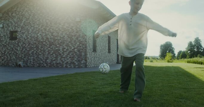 Boy having fun playing with a soccer ball in the backyard barefoot, summer evening