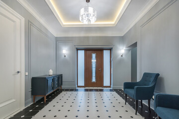 A spacious hall with a neoclassical entrance door in a luxurious mansion. The floor is .decorated with patterned tiles. Classic furniture of gray-blue color.