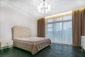 Laconic bedroom interior design. Double bed with high upholstered headboard, white .furniture, dark parquet.