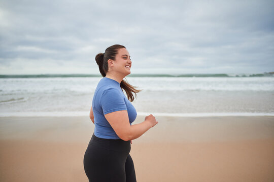 Motivated body positive sports woman jogging at the sandy sea beach