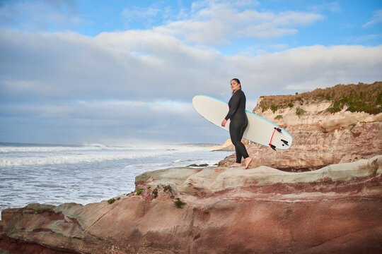 Full length view of the caucasian woman walking with surfboard at the rocky hill - Powered by Adobe