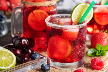 Red drink with ice. Raspberry, lime, strawberry, blueberry and mint leaves. Berry mojito in a misted glass.