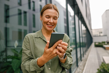 Stylish woman entrepreneur using phone whiile standing on modern building background 