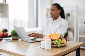 Selective focus of fresh fruits and medications being placed on writing desk at nutritionist's...