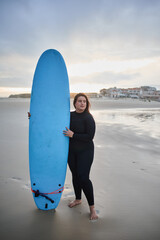 Calm full figured woman surfer carrying her surfboard and looking at the wavy ocean